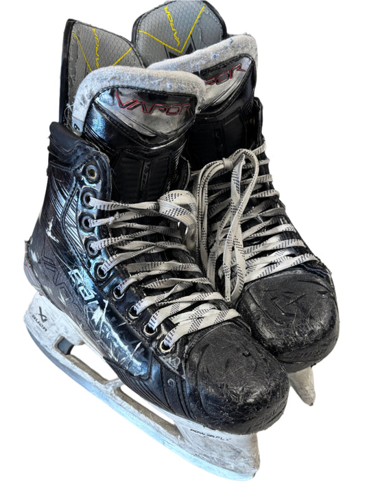 Pair of black hockey skates with white laces on a white surface.